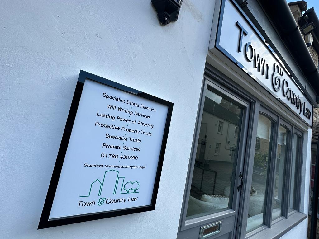 The framed services board mounted on the white render outside the Stamford Walk shopfront, listing the services and the 01780 430390 phone number