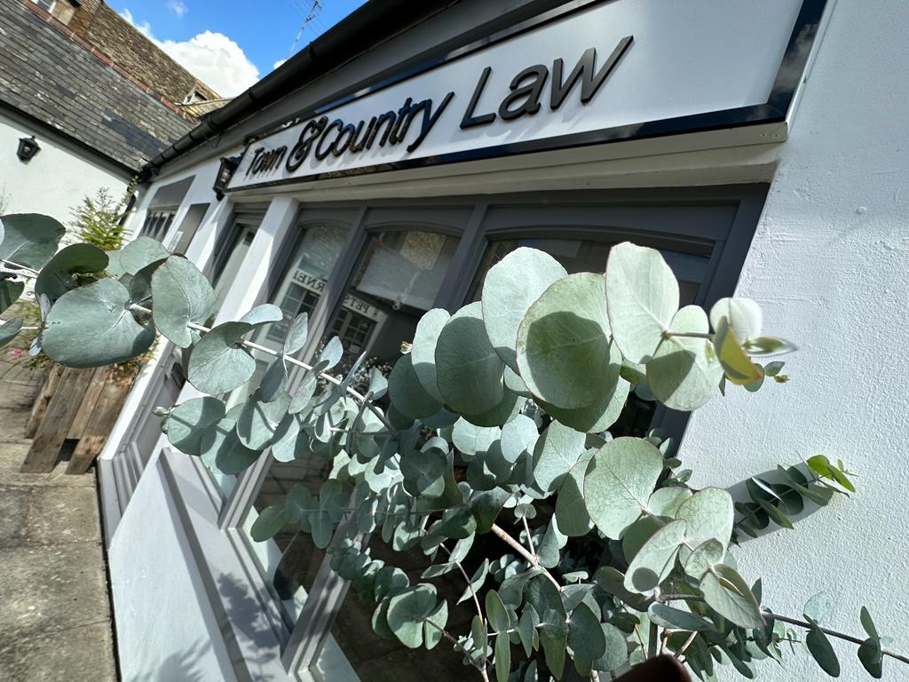 Town & Country Law shopfront on Stamford Walk, framed by eucalyptus leaves under a clear sky